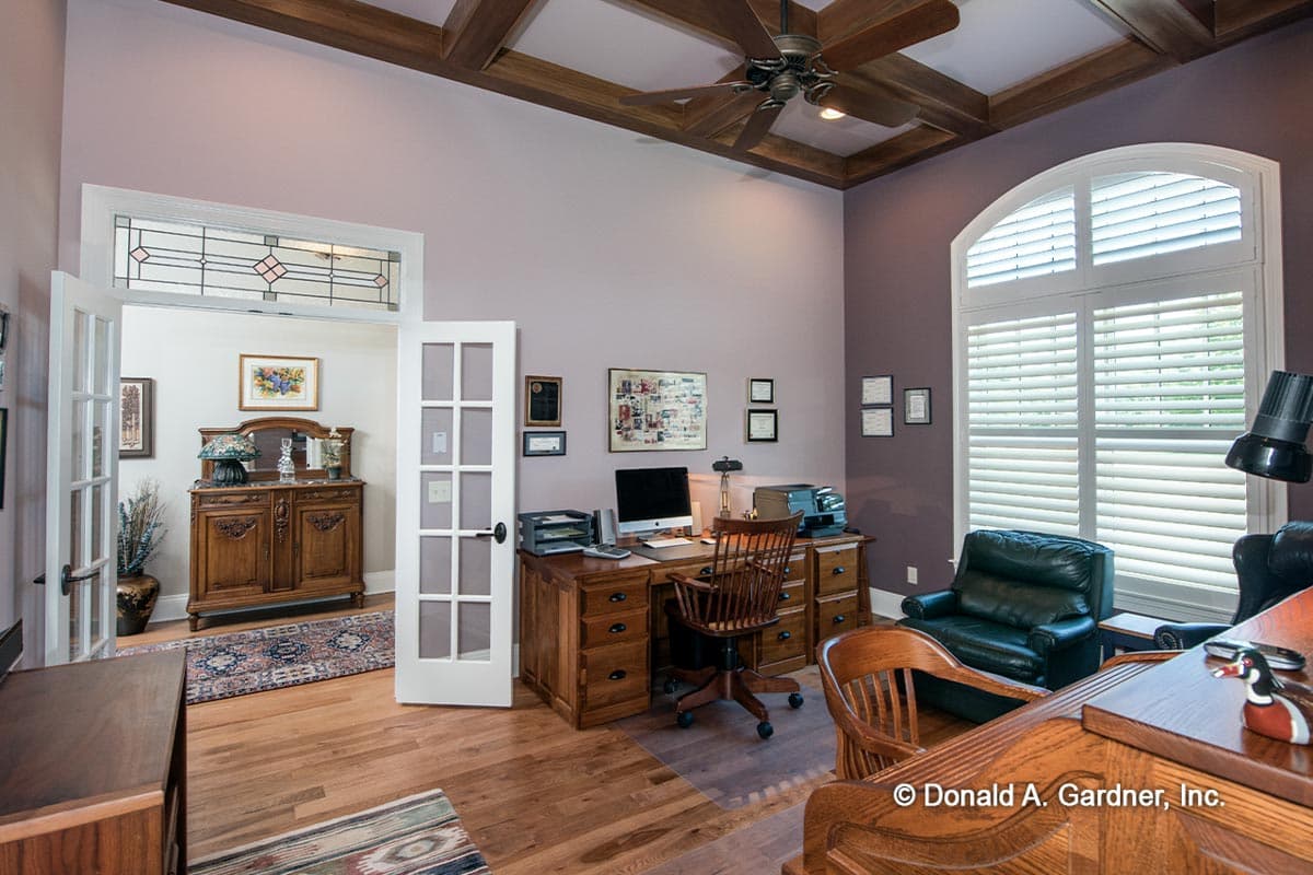 Office interior featuring a coffered wood ceiling, wood desk with computer, French doors, and arched plantation shutters.