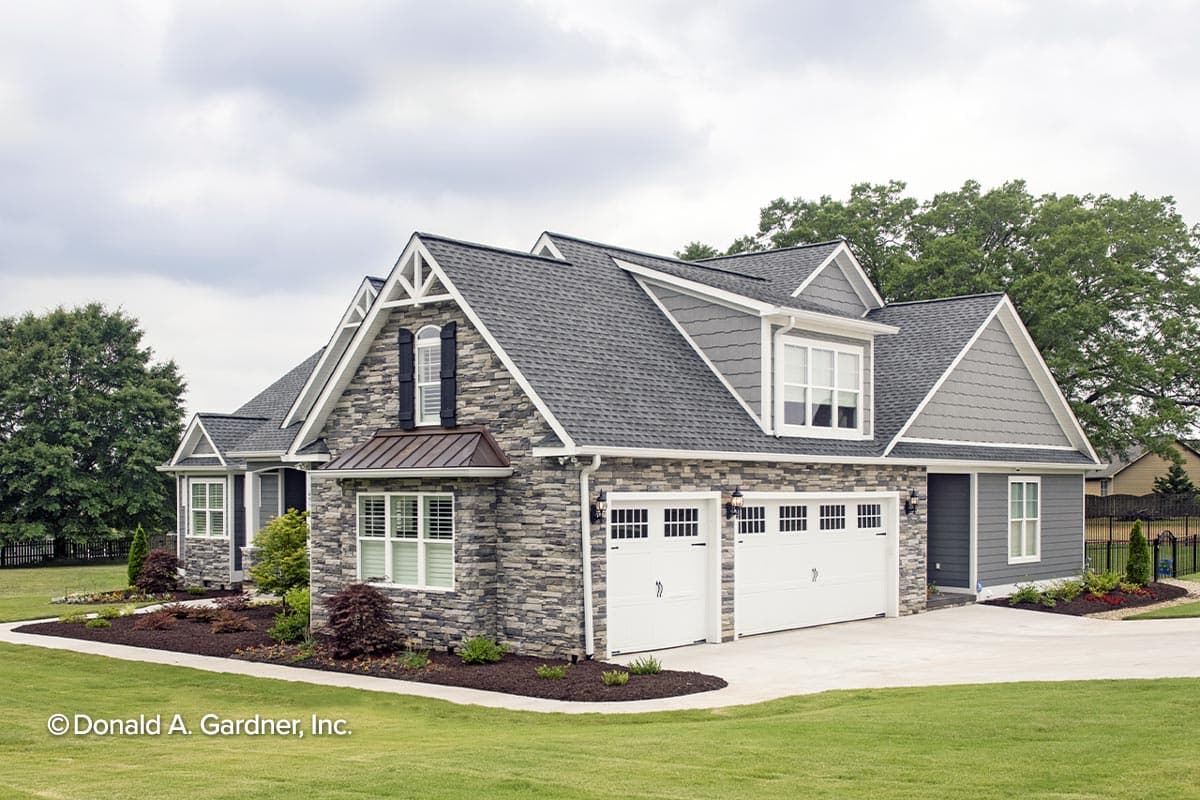 House plan exterior: Two-story home with stone front, multiple gables, dormer windows, and a three-car garage.