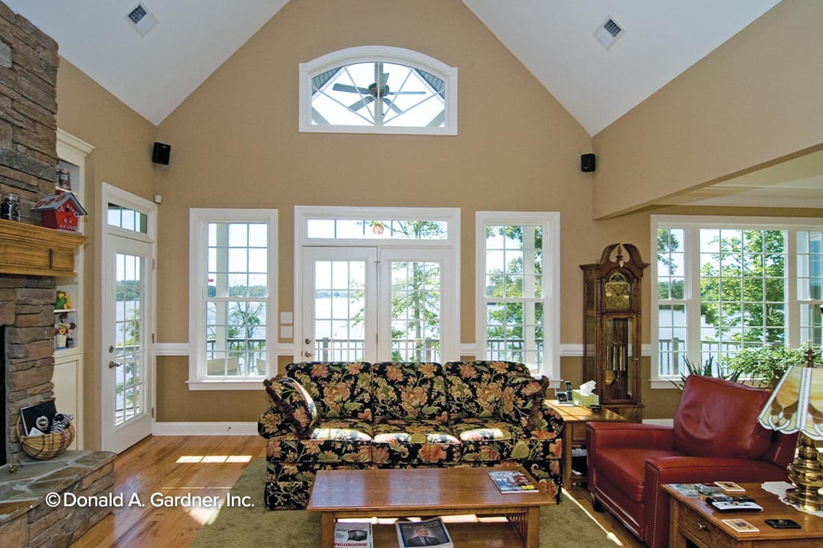 Living room with vaulted ceiling, stone fireplace, large windows, and French doors with lake view.