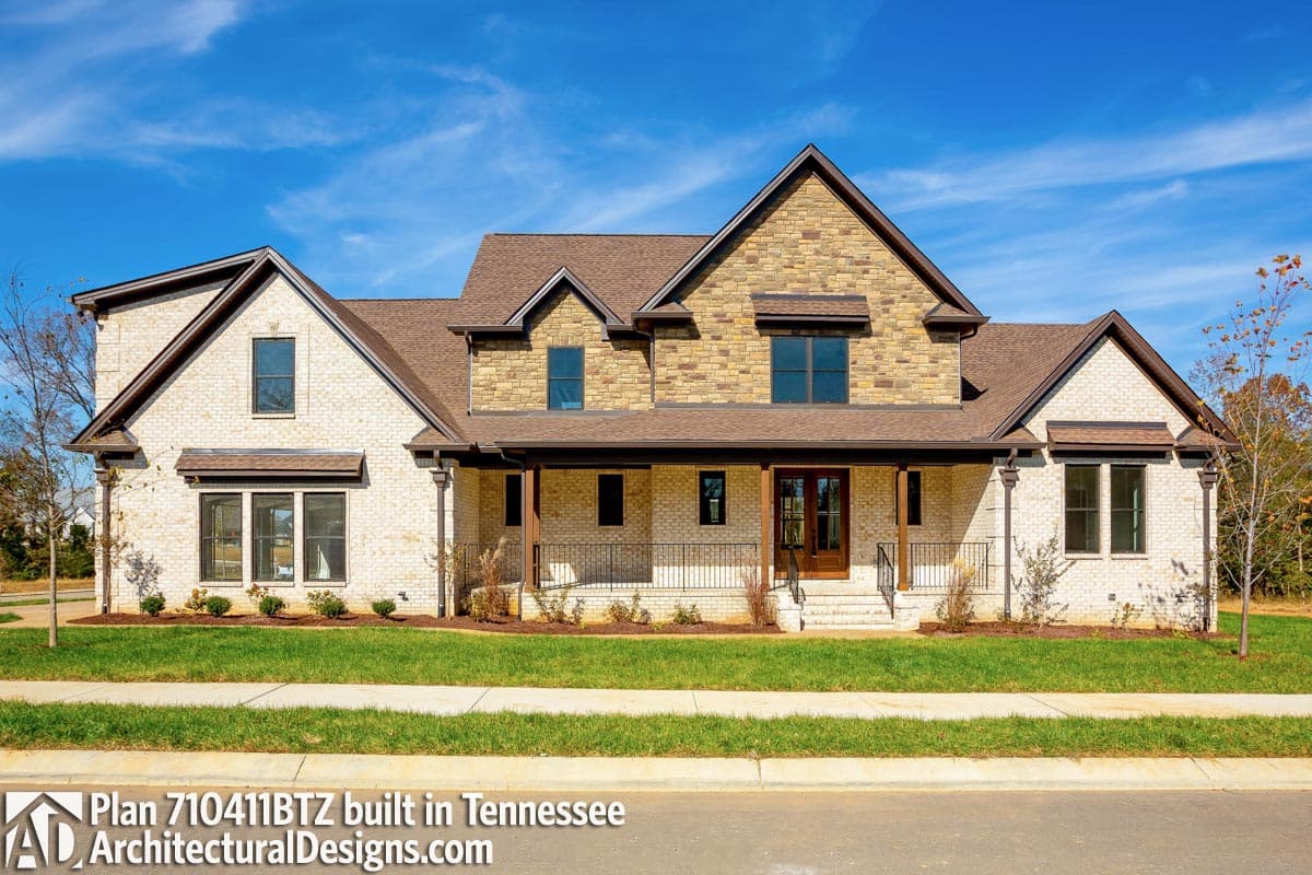 House plan exterior: two-story home with brick facade, stone accents, gable roof, covered porch, and multiple dormers.