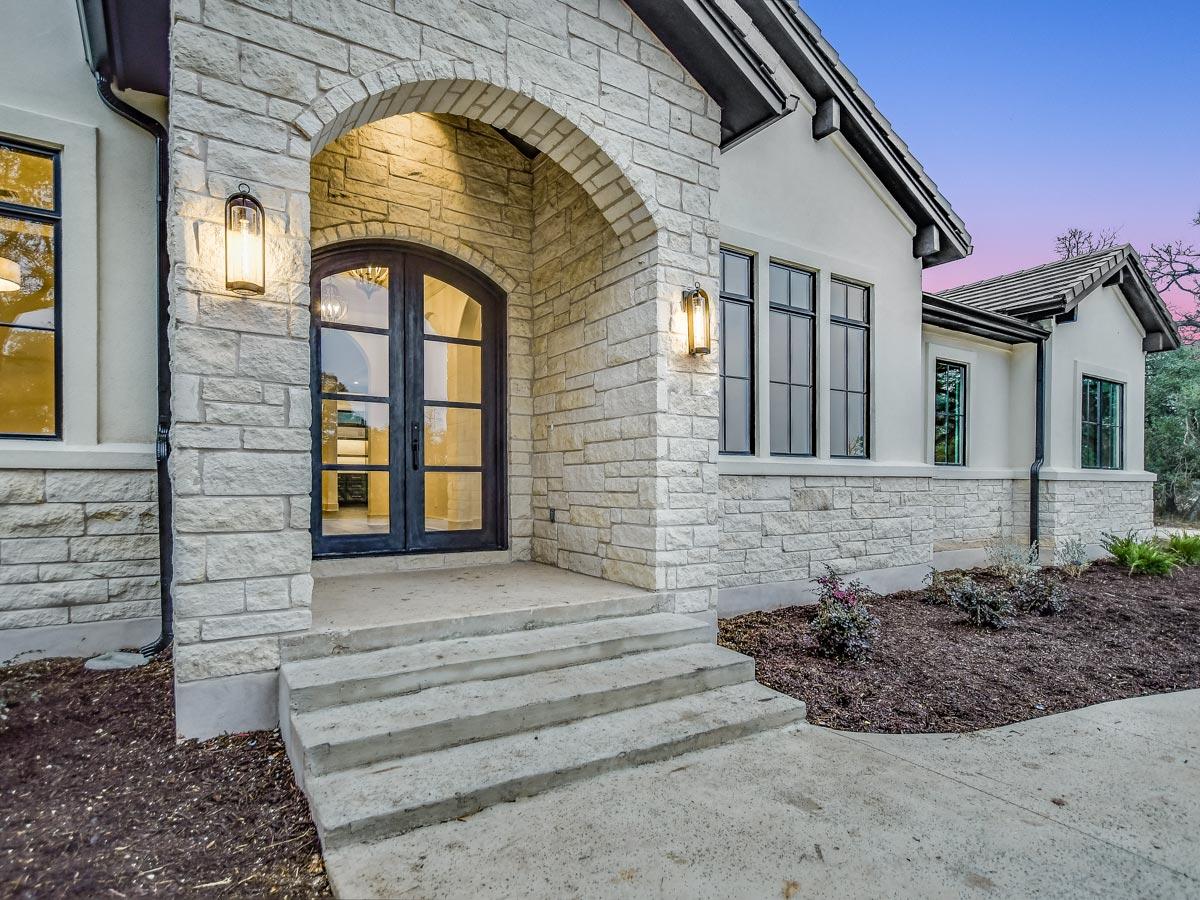 House plan exterior with stone facade, arched entry with double doors, and multiple gables.