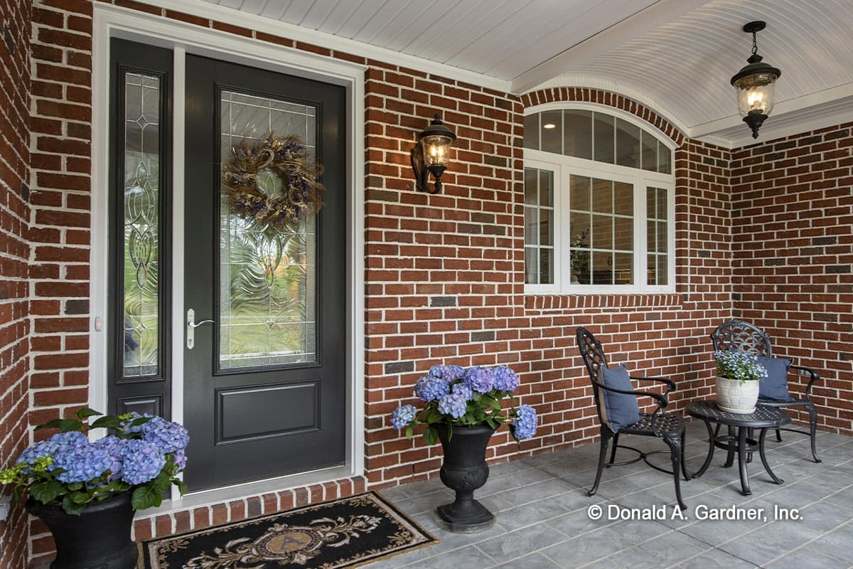 House plan exterior showing a dark front door with glass panels, arched window, and covered porch with seating.