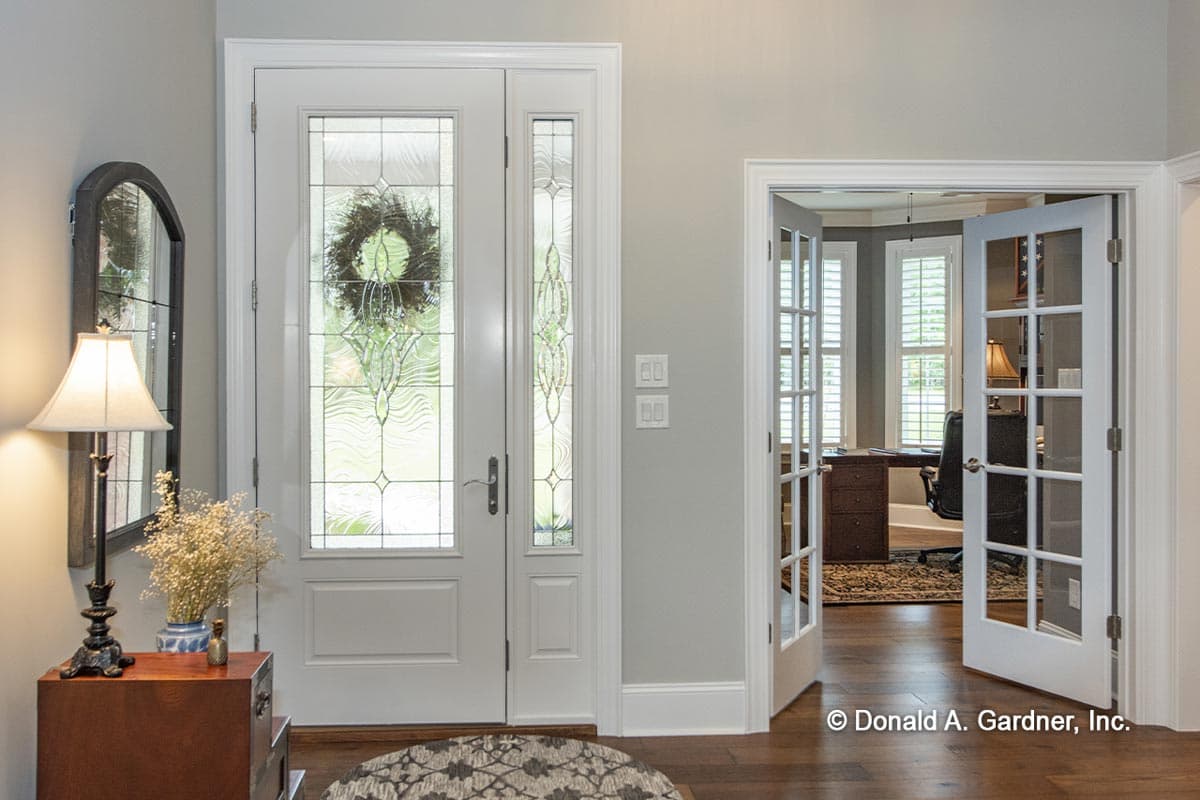 Double entry doors with decorative glass flank a room with glass-paned French doors, revealing a home office.