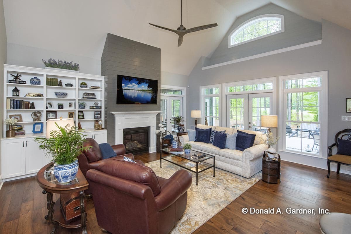 Great room with fireplace, built-in bookshelves, vaulted ceiling, and large windows. House plan rendering.