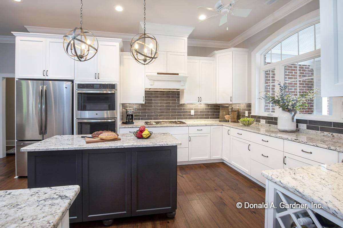Modern kitchen with dark island, stainless steel appliances, white cabinetry, granite countertops, and subway tile backsplash.