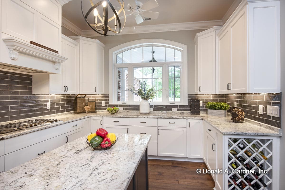 Kitchen interior with white cabinets, granite countertops, subway tile backsplash, and large arched window.