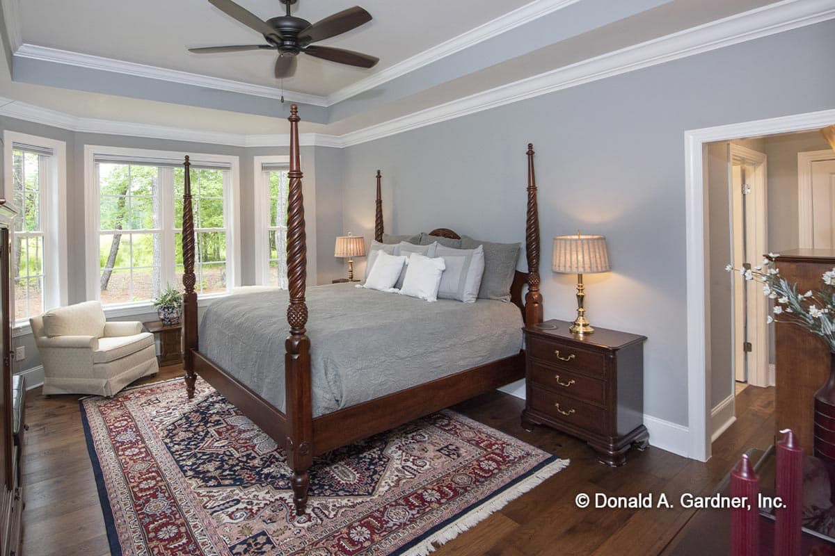 Primary bedroom with four-poster bed, tray ceiling, bay windows, and Persian rug.