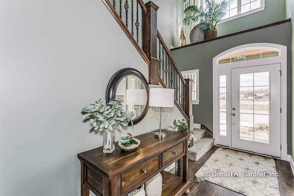 Entryway with a wooden console table, round mirror, and carpeted stairs leading to a second level.