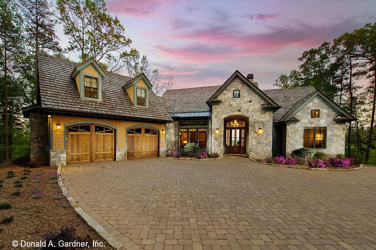 House plan exterior. Stone and wood exterior with multiple gables, shake roof, and dormers. Features include a two-car garage with wood doors.