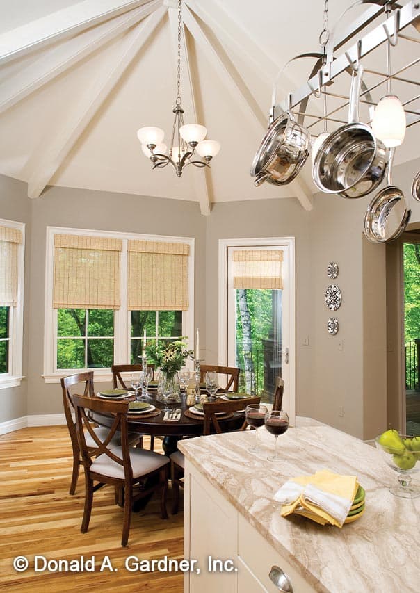 Interior view of a dining area with a vaulted ceiling, large windows overlooking trees, and a round dining table set for six.