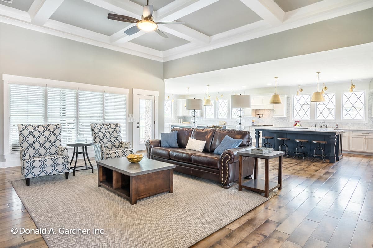 Living room with coffered ceiling, leather sofa, and island kitchen. Open layout.