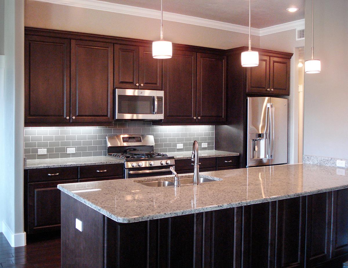 Modern kitchen with dark wood cabinets, granite countertops, stainless steel appliances, subway tile backsplash, and island.
