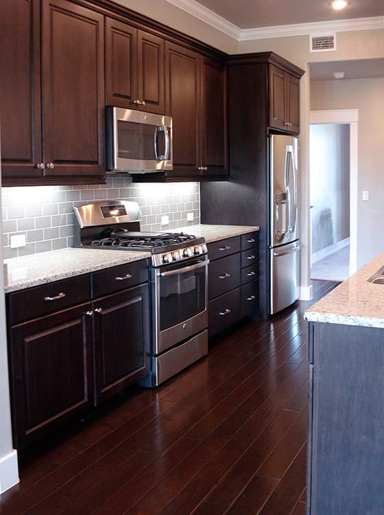 Kitchen interior with dark wood cabinets, stainless steel appliances, granite countertops, and subway tile backsplash.