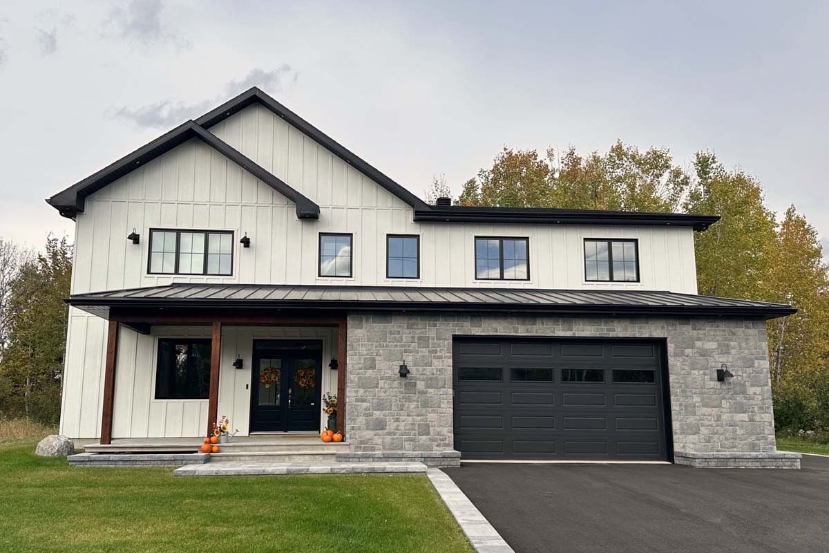 A modern two-story home with white siding, black accents, and a grey stone facade. Decorated for autumn with pumpkins and wreaths at the entrance.