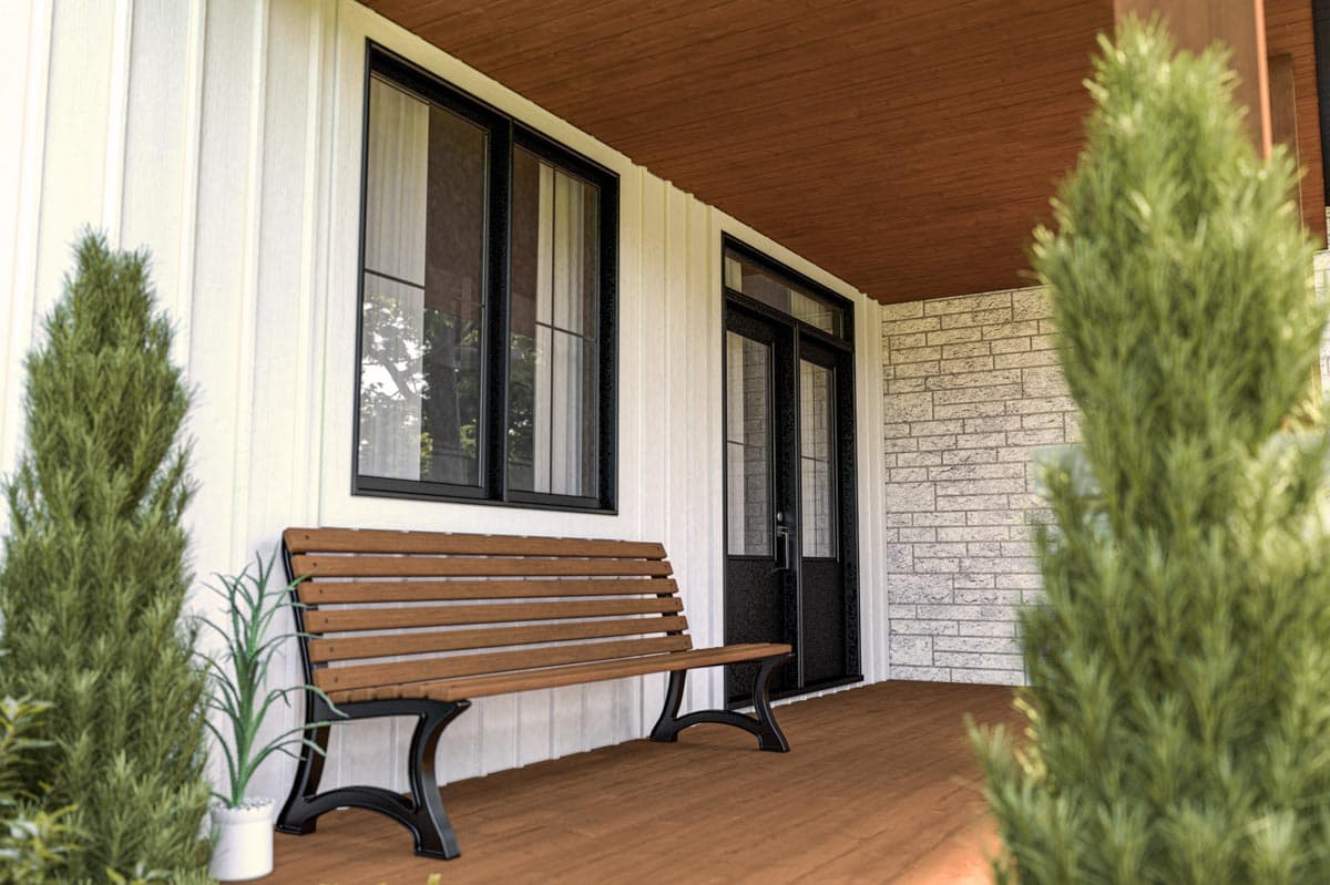 A covered porch with a wooden bench sits in front of a white building with black window and door frames. Green bushes frame the scene.