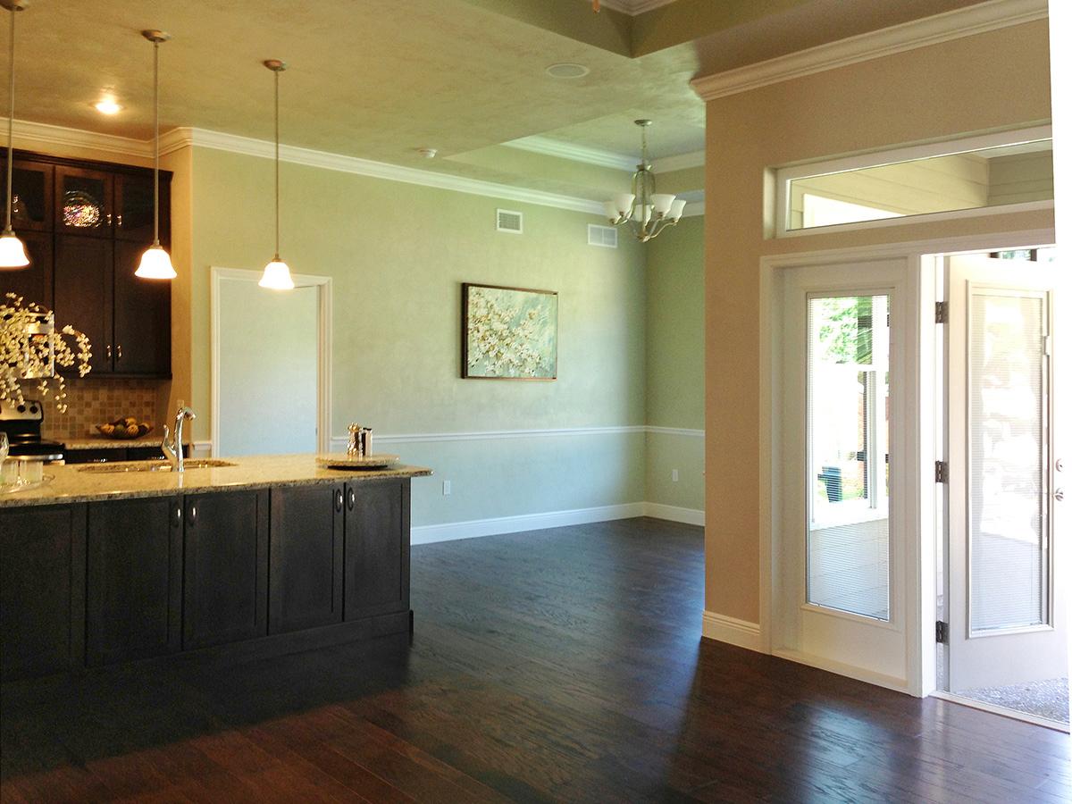 Kitchen island with pendant lights and dark cabinetry opens to a dining area with a chandelier and double doors.
