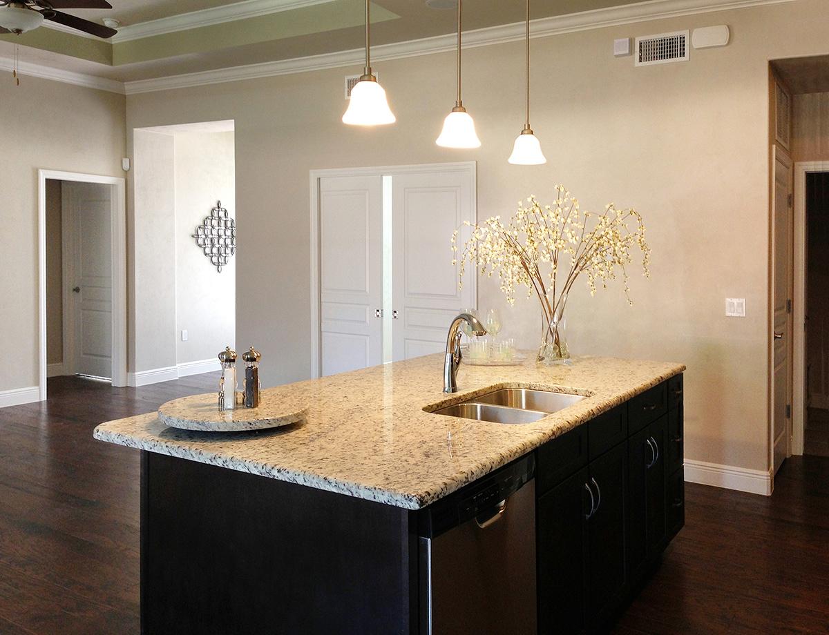 Kitchen island with granite countertop, stainless steel sink and faucet, and dark cabinetry. Open doorway to adjacent room.