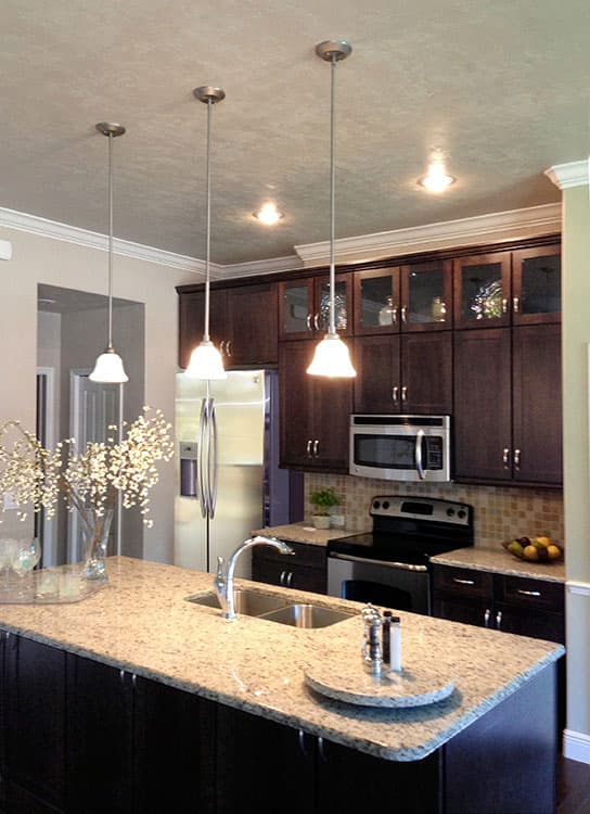 Kitchen interior with granite-topped island, dark wood cabinets, stainless steel appliances, and pendant lights.