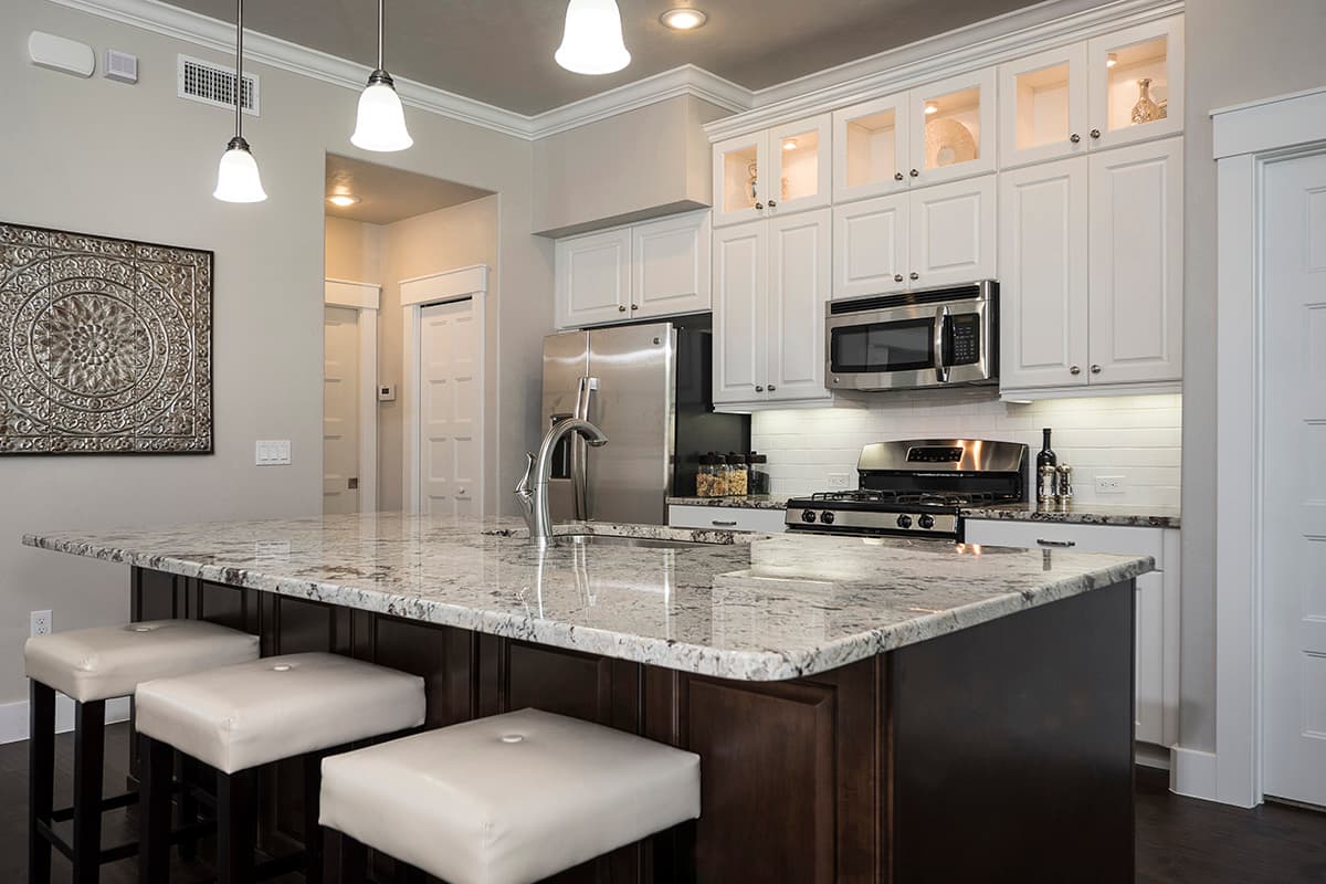 Kitchen with granite island, white cabinets, stainless steel appliances, and pendant lighting.
