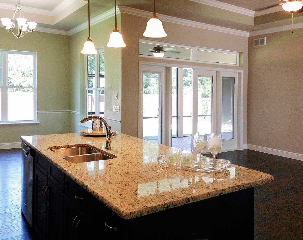 Kitchen island with granite countertop, undermount sink, and faucet. Views of windows and glass doors.