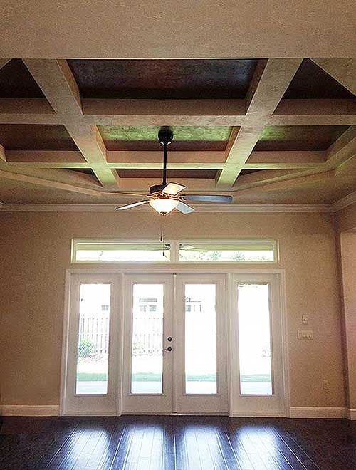 Interior view showing a coffered ceiling with a fan and glass double doors leading outside.