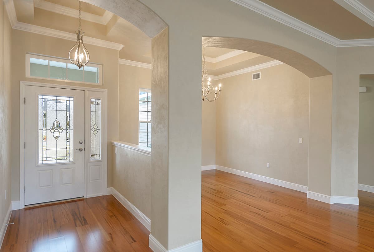 Interior view of a house entrance with a double door featuring decorative glass, leading to a dining area with hardwood floors.