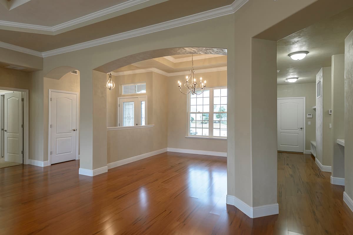 Interior view showing dining area with tray ceiling, arched entryway, and chandelier, leading to hallway with doors.