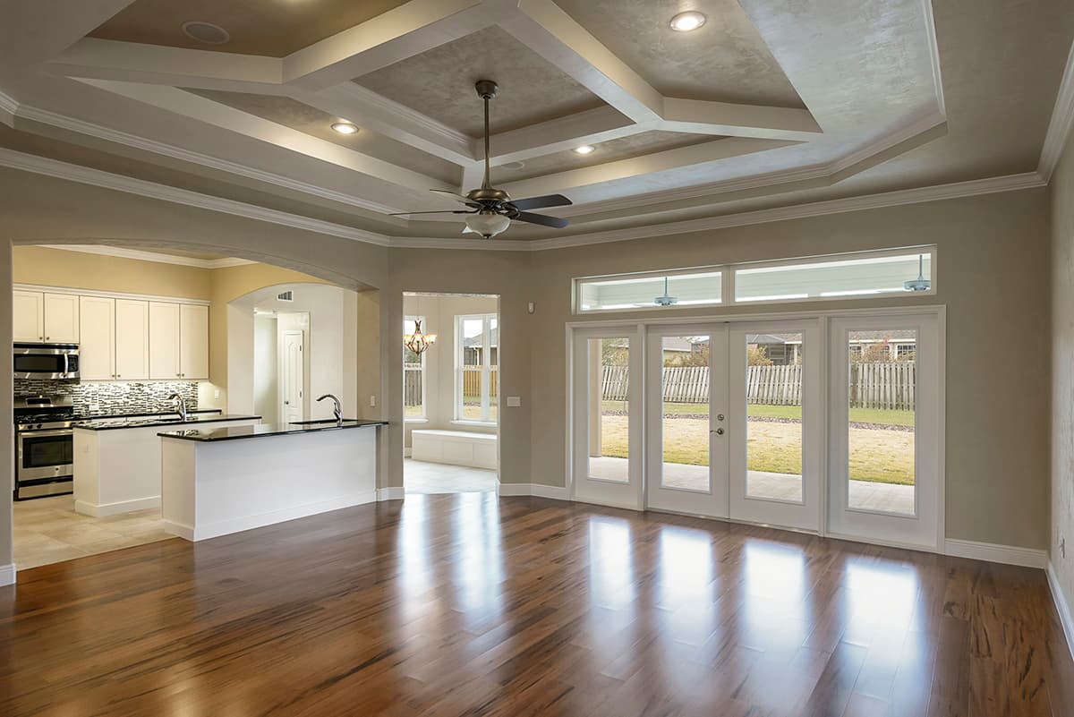 Interior view showing kitchen with island, great room with coffered ceiling and French doors leading to backyard.