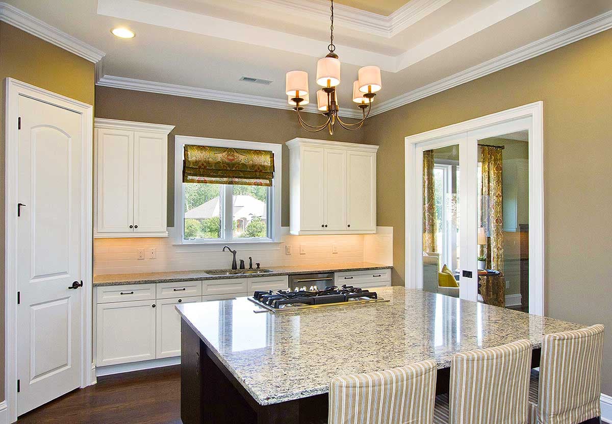 Kitchen with island cooktop, white cabinetry, granite countertops, and coffered ceiling.
