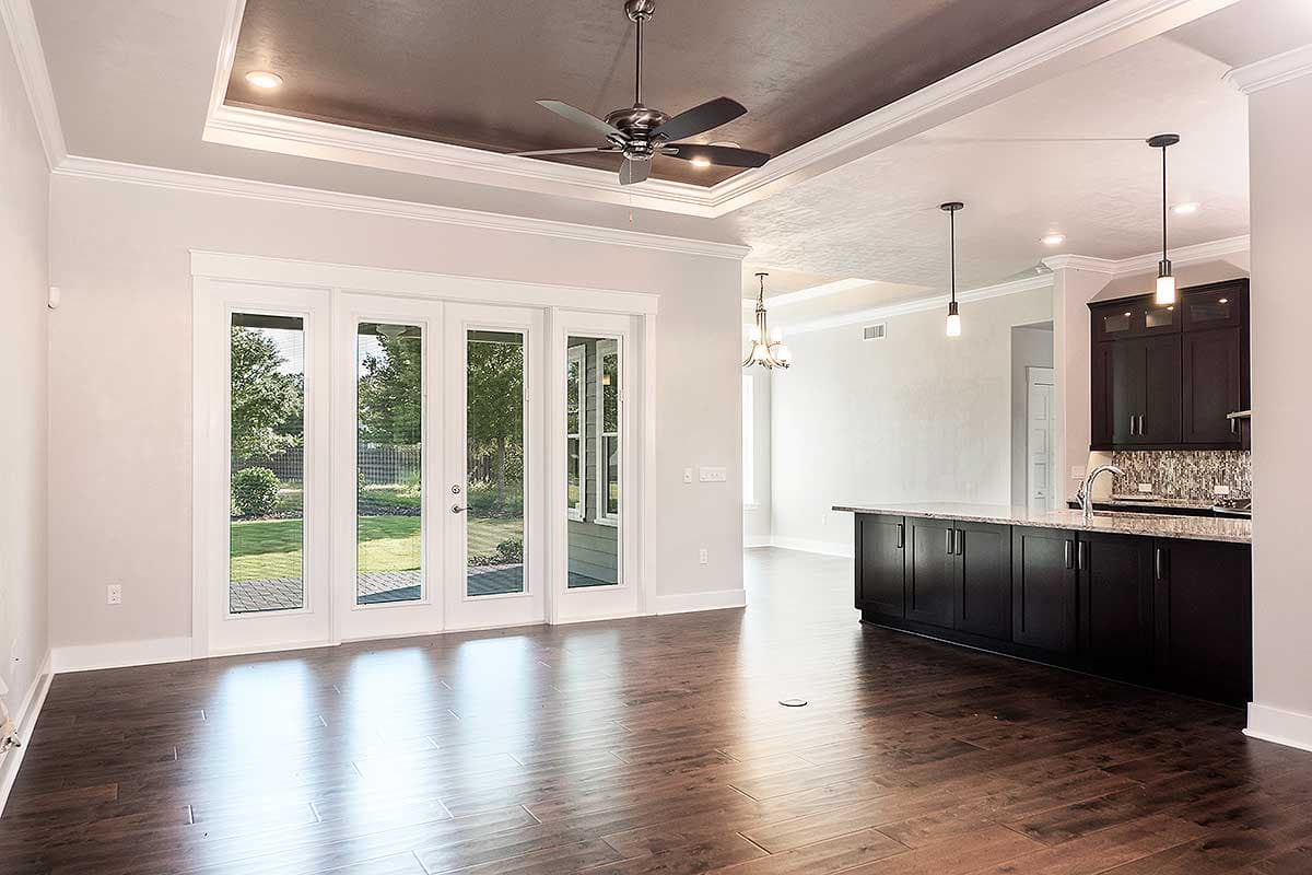 Interior rendering of an open concept living space featuring French doors, a kitchen island with dark cabinetry, and a tray ceiling with a fan.