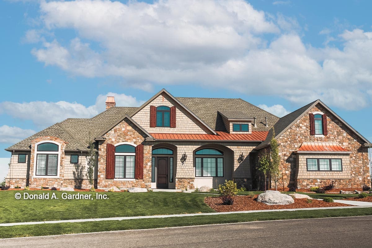 House plan exterior with stone veneer, gabled roof, and arched windows. Features include copper accents and multiple dormers.
