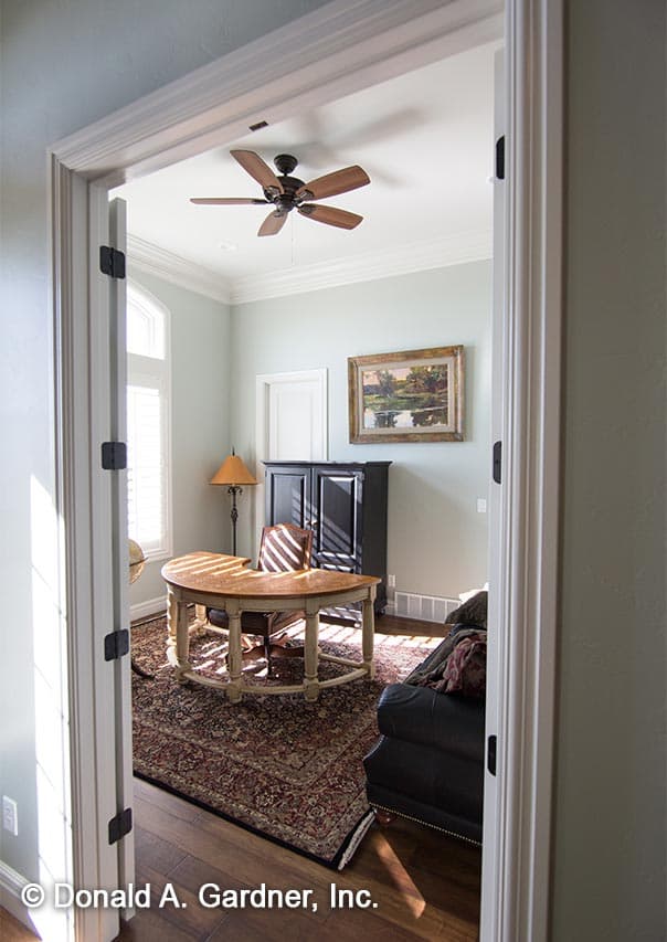 Interior view of home office with curved desk, dark cabinet, fireplace, and ceiling fan.