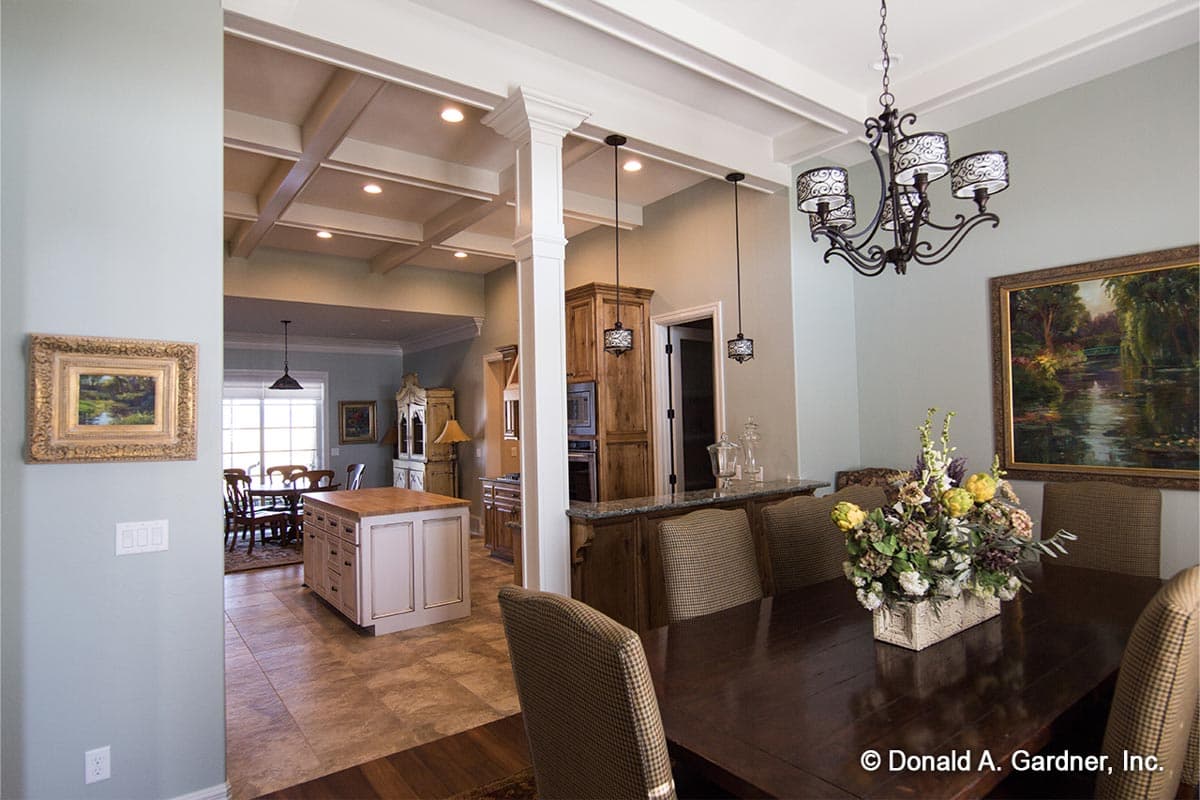 Interior view of a dining room and kitchen with coffered ceiling, island, wood cabinets, and chandelier.