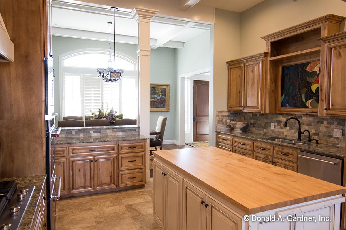 Kitchen with wood cabinetry, granite countertops, large island with butcher block top, and arched window.