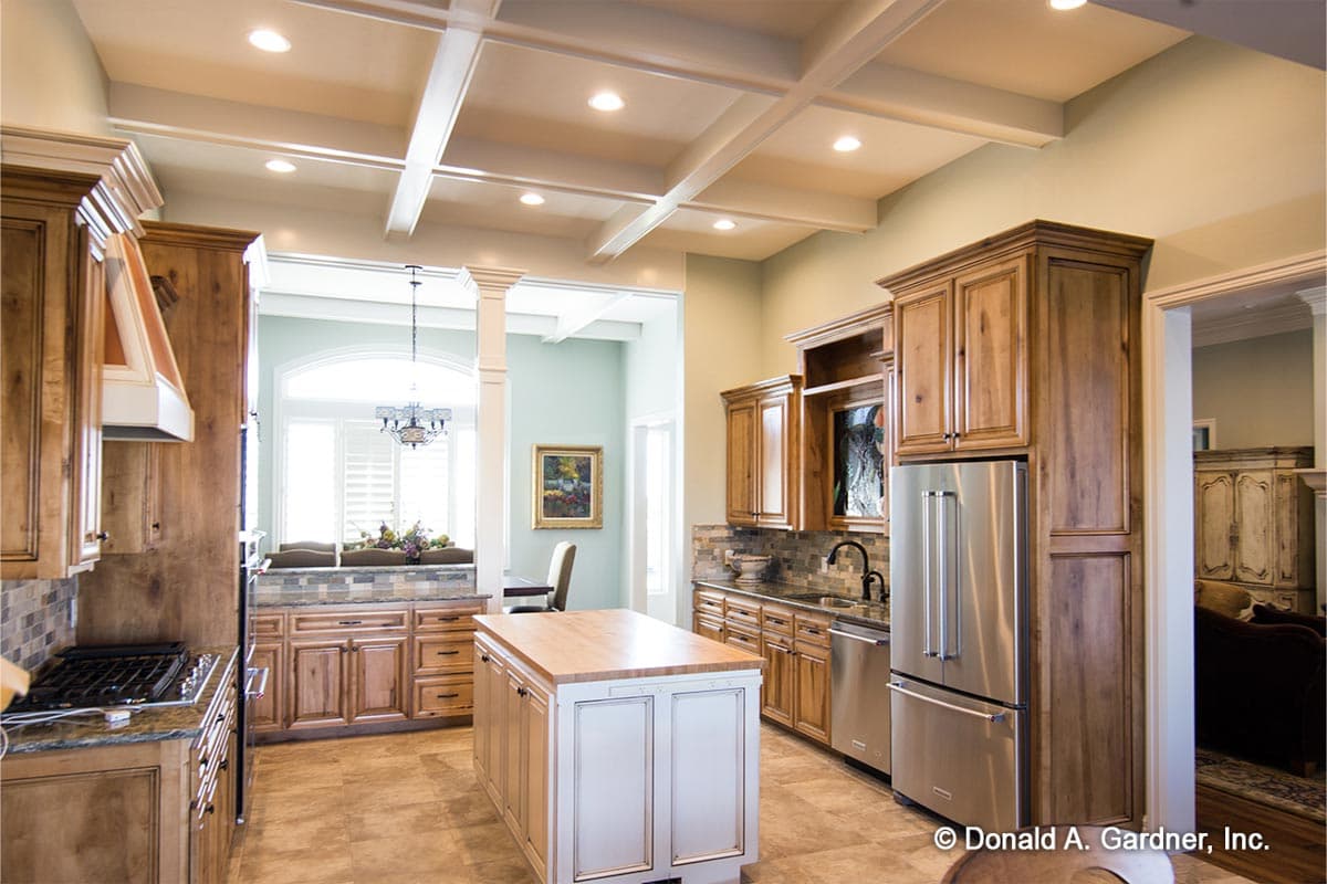 Kitchen interior with coffered ceiling, wooden cabinets, island, stainless steel appliances, and large arched window.