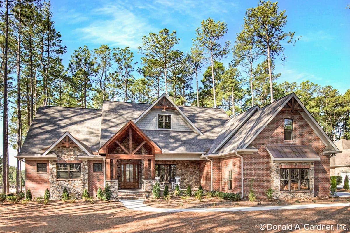 House plan exterior. Craftsman style, one-story. Features include a covered porch with exposed beams, brick and stone facade, and multiple gables.