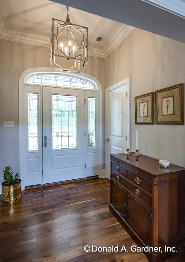 Foyer interior featuring an arched transom window, leaded glass sidelights, a central door, hardwood floors, and a decorative chandelier.