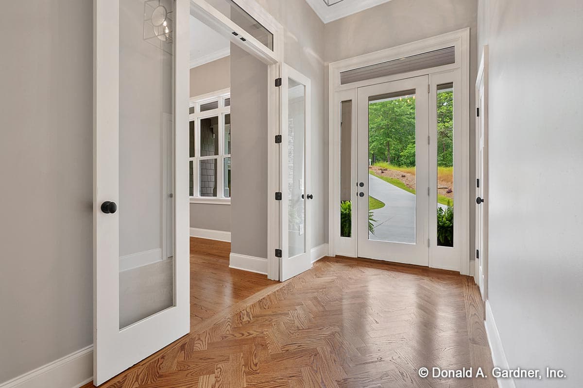 Interior view of a house entrance with double glass doors, interior glass doors, and herringbone wood floors.
