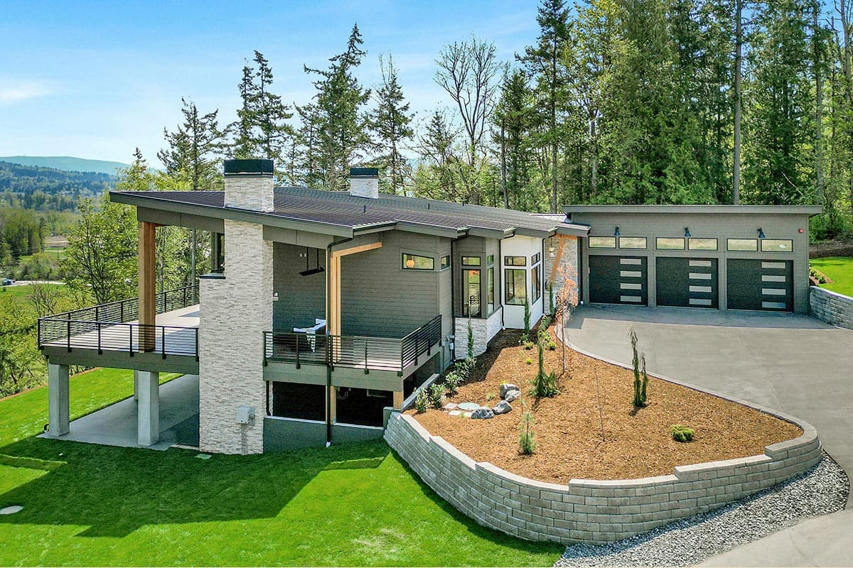 Modern house plan exterior with a cantilevered deck, stone chimney, and a three-car garage with frosted glass panels.
