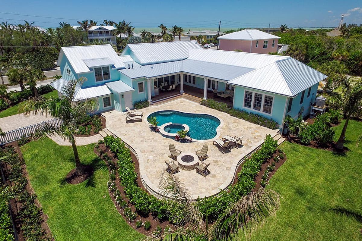 Two-story house plan exterior with a light blue facade, L-shaped footprint, gabled rooflines, and a central courtyard with a pool.