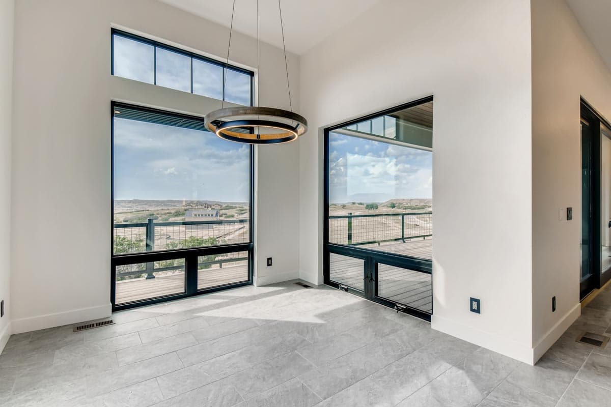 Interior view with high ceilings and large windows overlooking a deck and landscape. Modern light fixture hangs centrally.