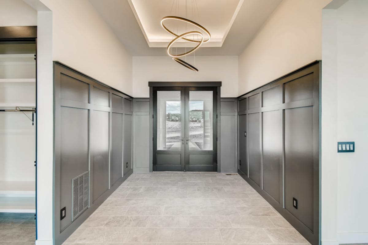 Entryway with wainscoting, double glass doors, tiled floor, and modern pendant light.
