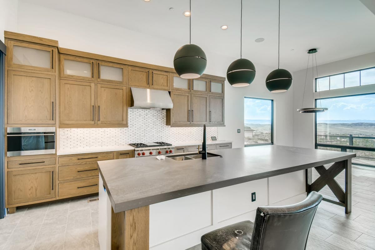 Modern kitchen featuring a large island with a sink, wood cabinetry, stainless steel appliances, and a geometric tile backsplash.