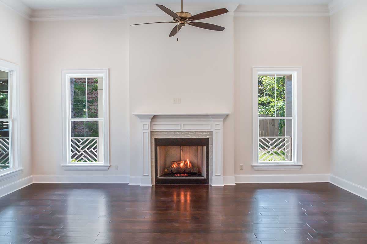 Living room with fireplace, ceiling fan, and windows with decorative grilles. Dark wood floors.
