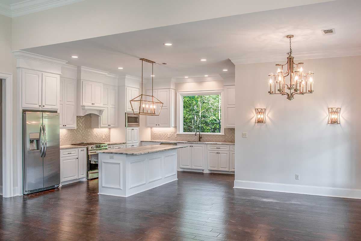 Kitchen with white cabinetry, large island, stainless steel appliances, and a wide window overlooking trees.