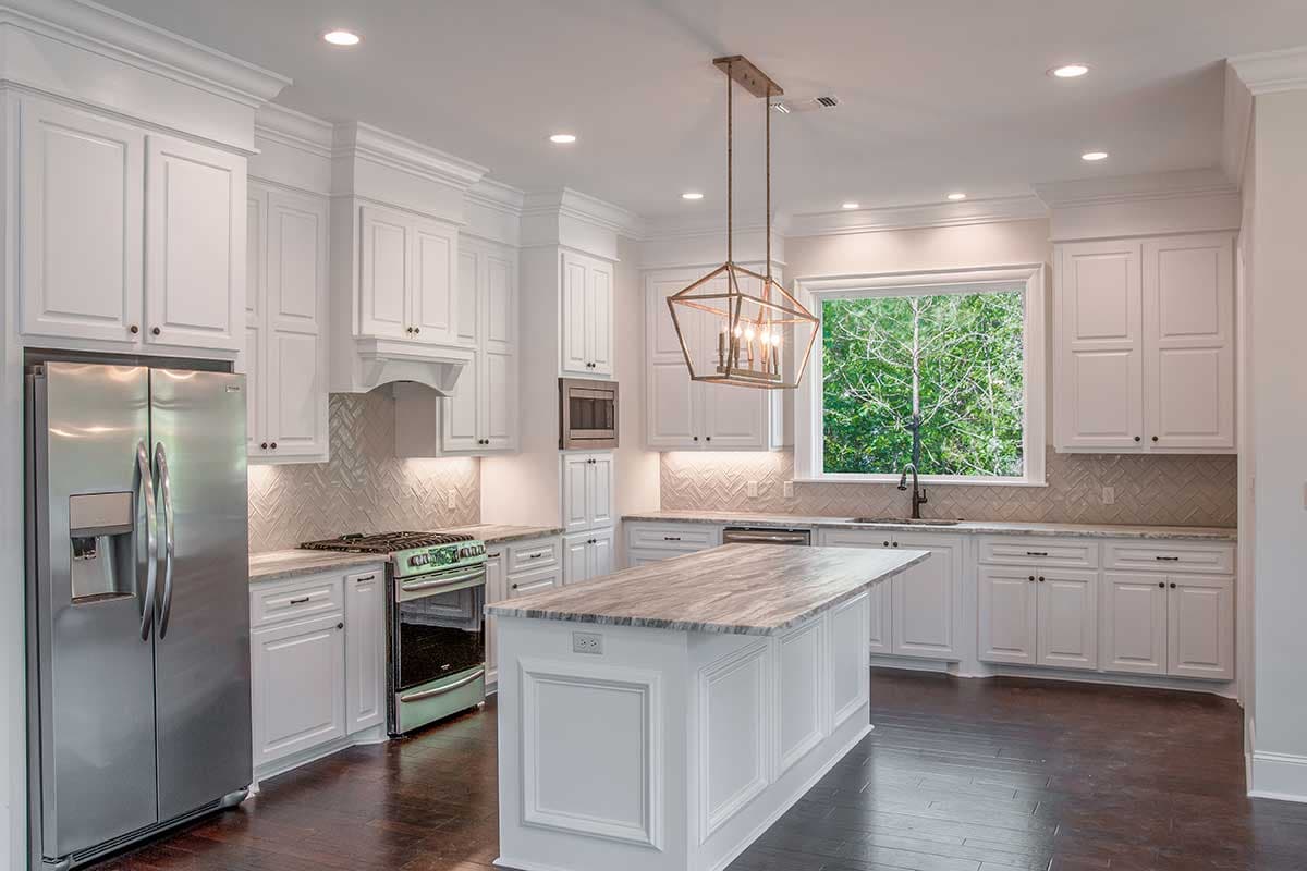 Kitchen with white cabinets, marble island, stainless steel appliances, and a large window overlooking trees.