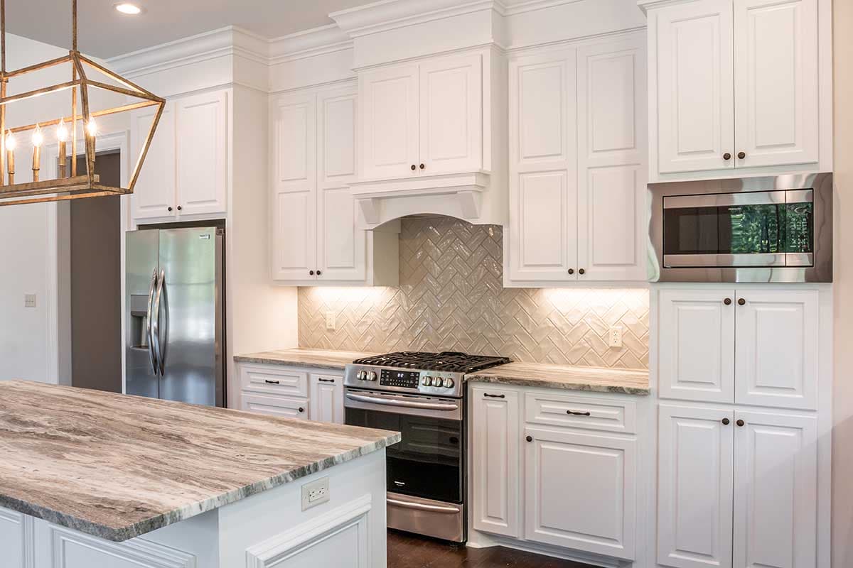 White kitchen with white shaker cabinets, stainless steel appliances including a built-in microwave, gas range, and island with granite countertop.