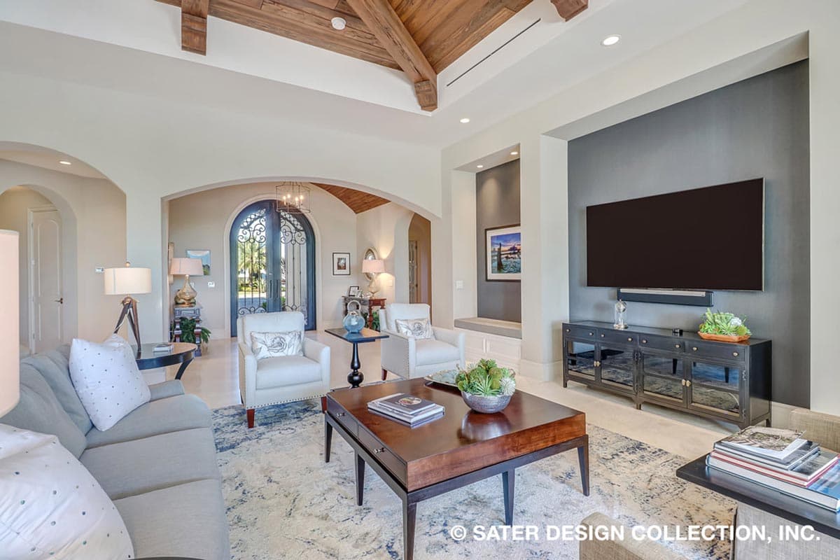 Interior view of a great room with vaulted wood-beamed ceiling, arched entryway, and media wall.