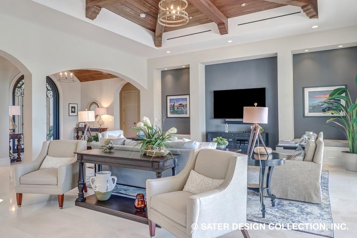 Interior view of a living room with exposed wooden beams on the ceiling, arched doorways, and a wall-mounted television.