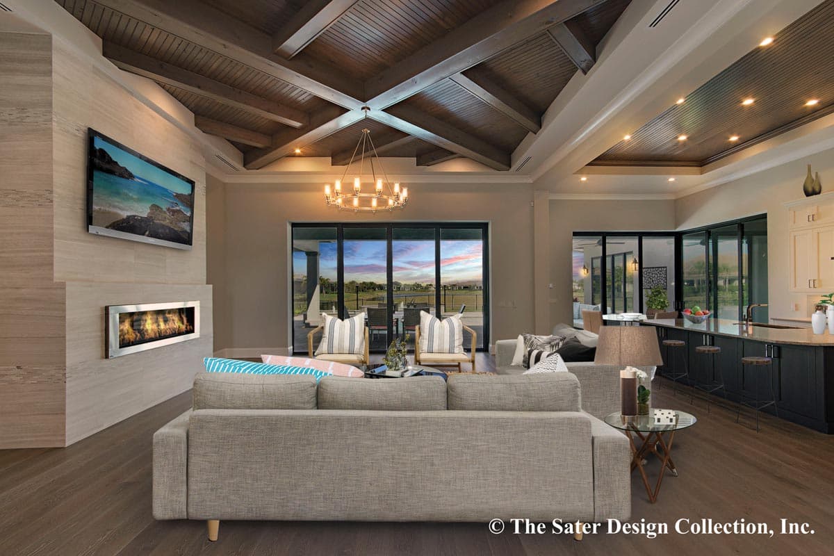 Living room with vaulted wood-beamed ceiling, modern fireplace, and open kitchen with island.